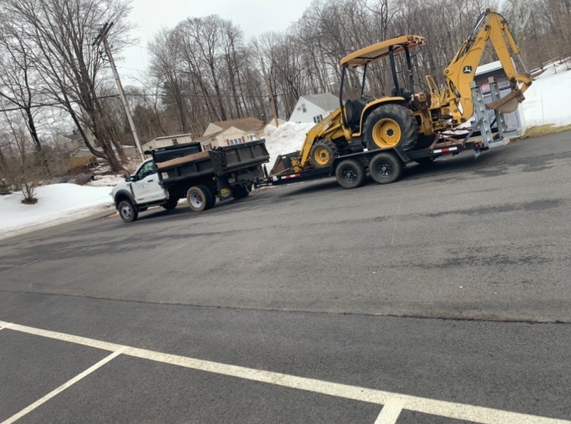 Country Hill dump truck hauling a backhoe loader on a flatbed trailer between job sites