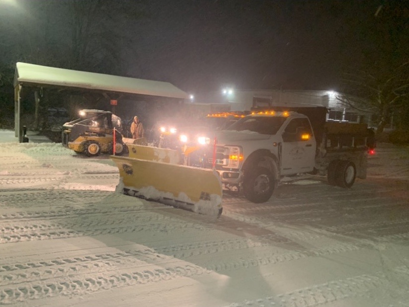 Plow truck and skid steer clearing snow at night during a Shoreline storm